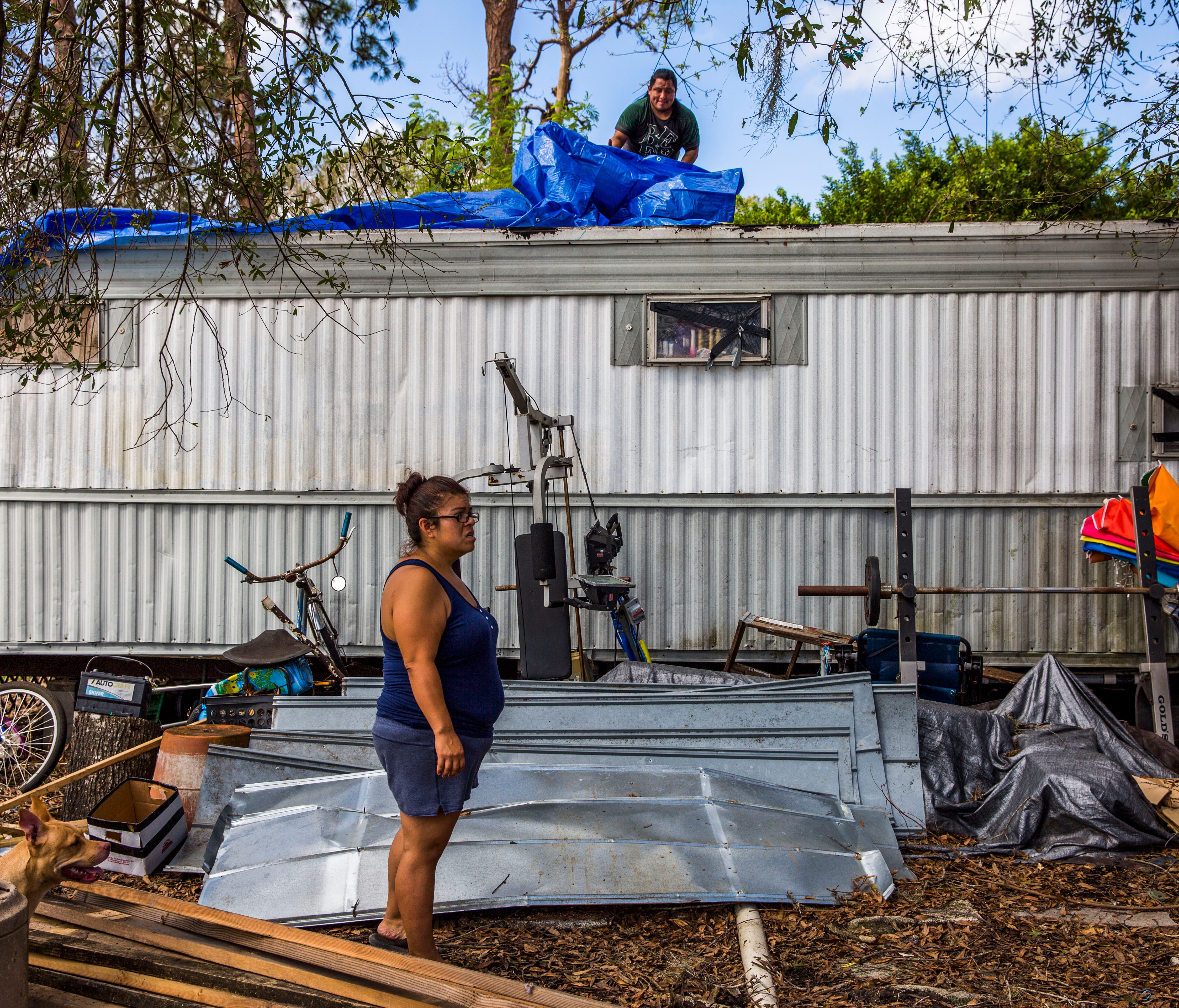 Samantha Tindell stands outside her damaged Immokalee trailer as her partner Antonio Martin puts a tarp over the roof Saturday, Sept. 23, 2017. Tindell and her partner and two children had been sleeping in a tent due to damage and mold in their home,