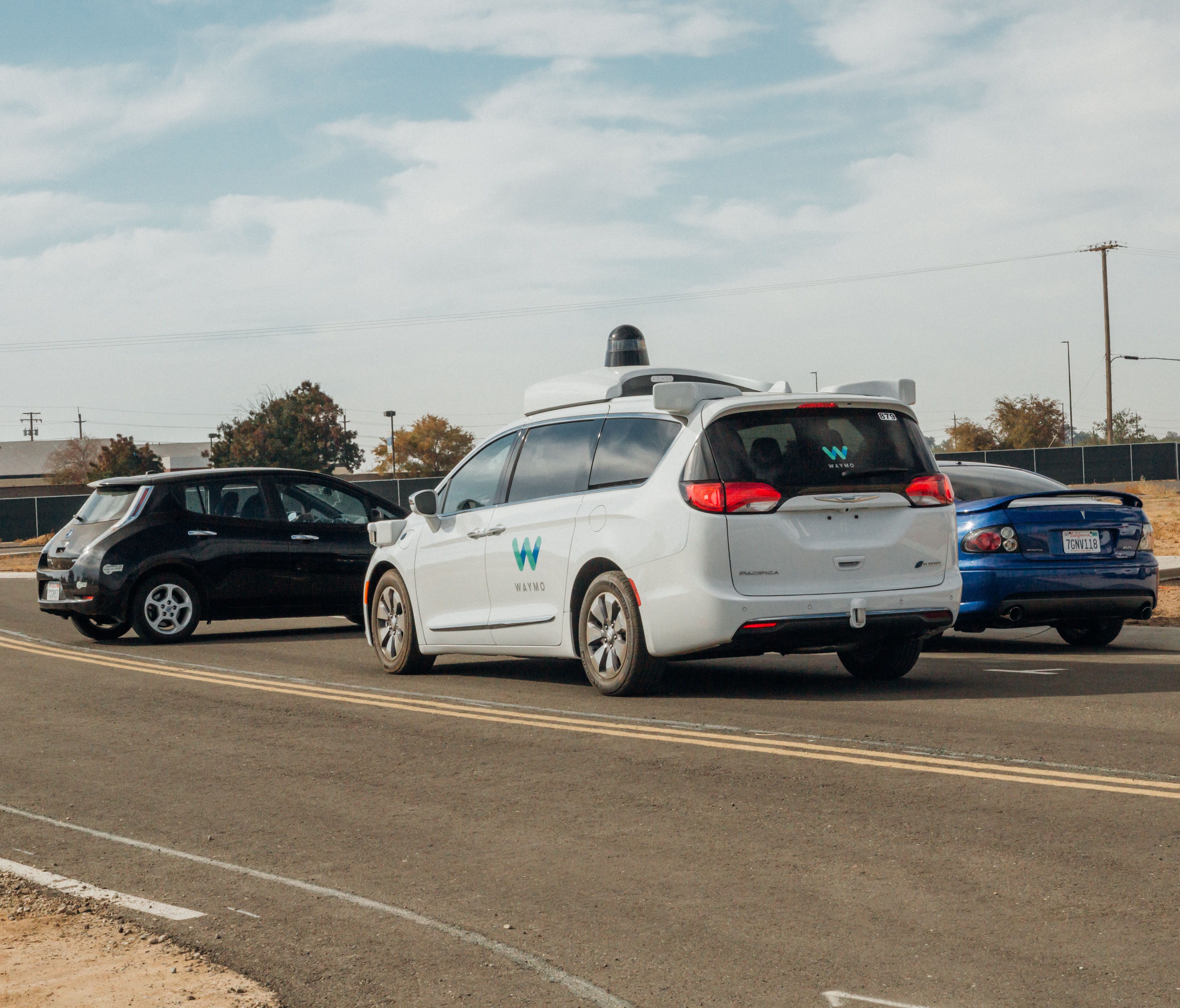 A Waymo minivan outfitted with self-driving sensors brakes suddenly for a black car that has backed out of a driveway without looking. The test was conducted at Waymo's testing facility in central California.