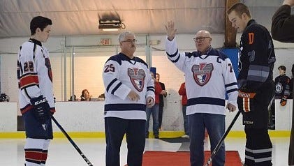 Livonia Franklin's 1973-74 captain, Dan Longeway (74) waves to the crowd before he and longtime Patriots coach Terry Jobbitt (25) each drop a ceremonial first puck Dec. 1 at Devonaire Ice Arena. Flanking them are current Franklin co-captain Jonah Pollack (22) and Dearborn Unified captain Andrew White (23).