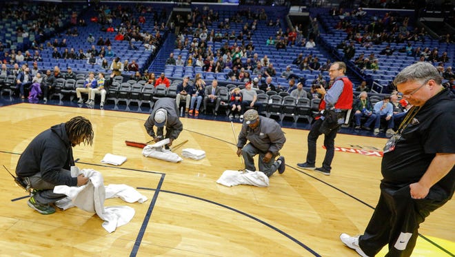 New Orleans Pelicans equipment manager David Jonanovic (right) inspects the court during a delay due to moisture on the floor from a roof leak before the start of a game between the New Orleans Pelicans and the Indiana Pacers at the Smoothie King Center.