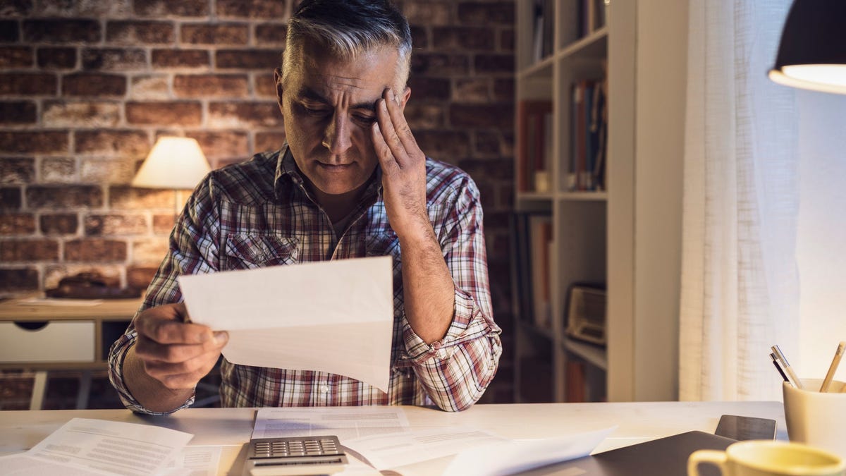 Older man holding his head while reading document, sporting worried expression