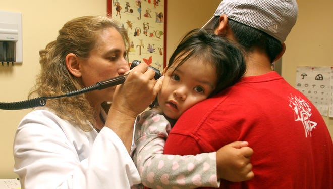 A pediatrician at Zufall Health Center in Dover, looks in the ear of a young patient.