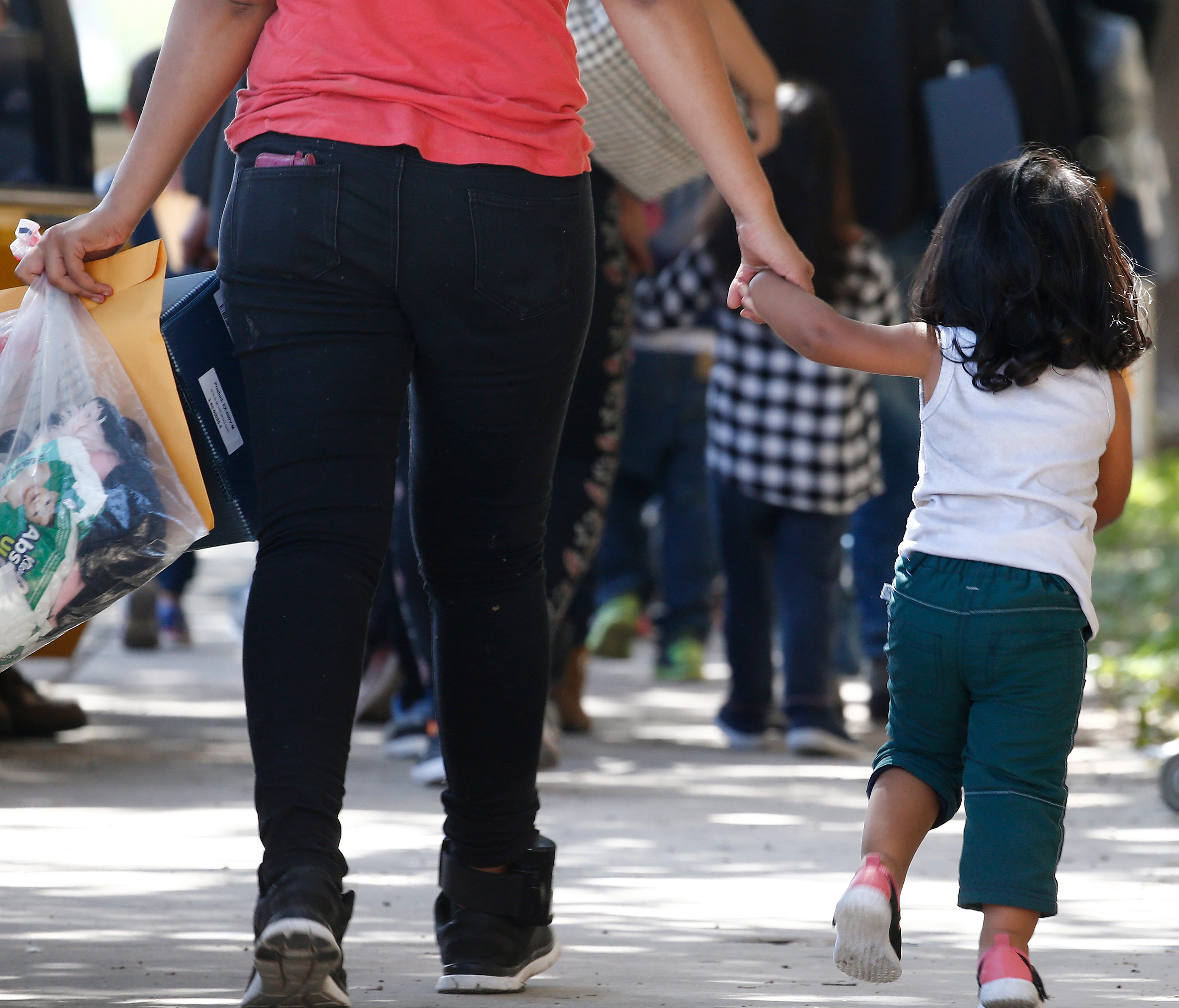 A little girl and a woman along with other migrant families cross the street after being processed at the Central Bus Station before being taken to Catholic Charities before being removed in McAllen, Texas 26 June 2018. Immigration along the Rio Gran