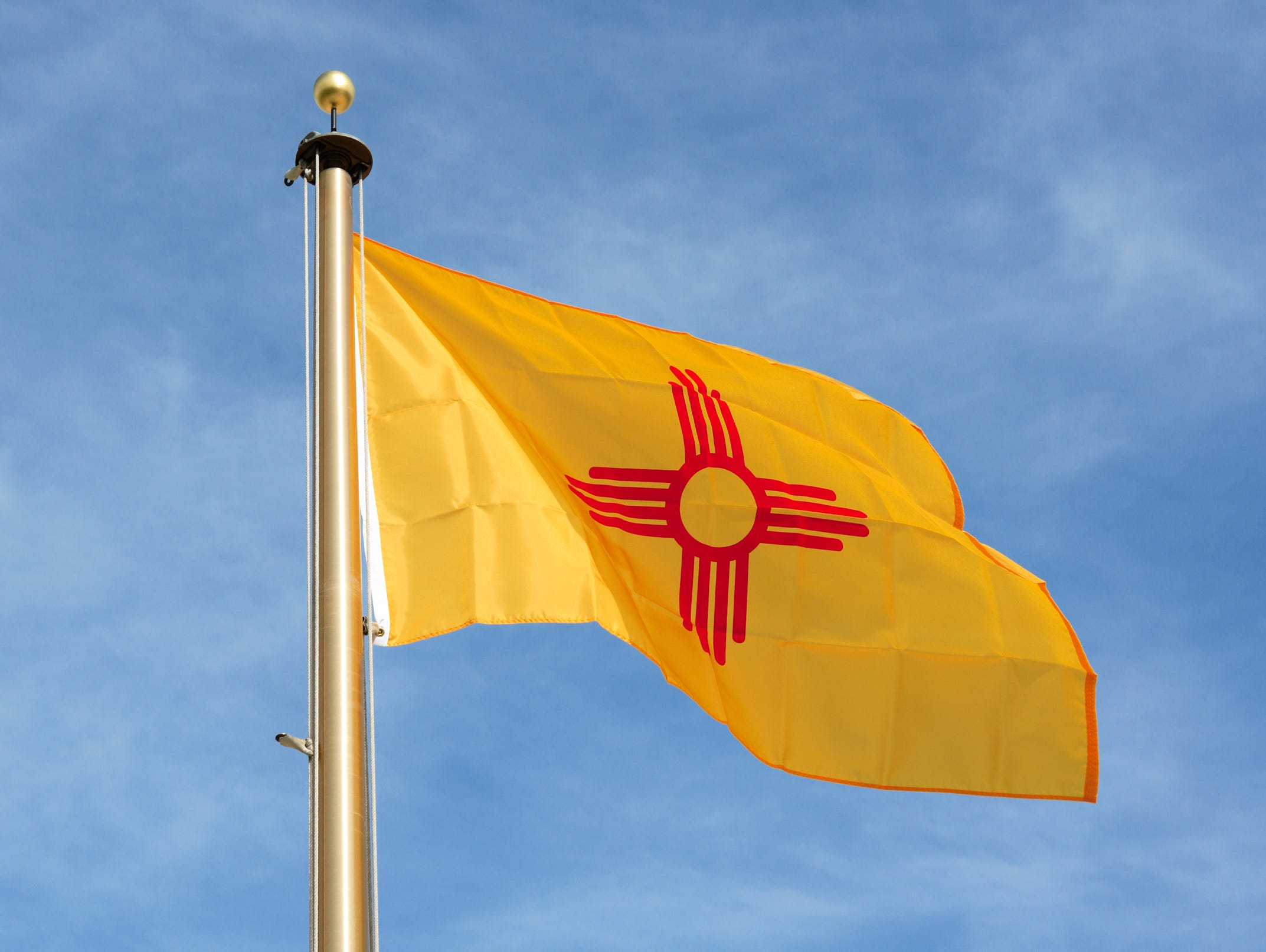New Mexico - In a common theme relating to state flags, the Daughters of the American Revolution encouraged the modern design of the New Mexico flag. It has a red sun symbol on a background of bright yellow. It is one of only four states to not have 