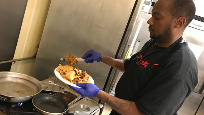 Line cook Sherman Foster spoons slow-roasted brisket chili atop nachos as a base for one of the restaurant’s new menu items, smokin’ nachos.