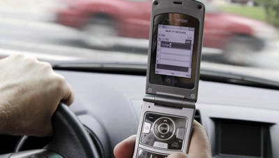 In this Sept. 20, 2011 file photo, a phone is held in a car in Brunswick, Maine. Americans are significantly less worried about drunk, aggressive and drowsy driving than they were four years ago even though traffic deaths have begun to edge back up, according to a survey by the AAA Foundation for Traffic Safety. At the same time, most Americans consider texting while driving completely unacceptable behavior, although one in four admit doing so recently.