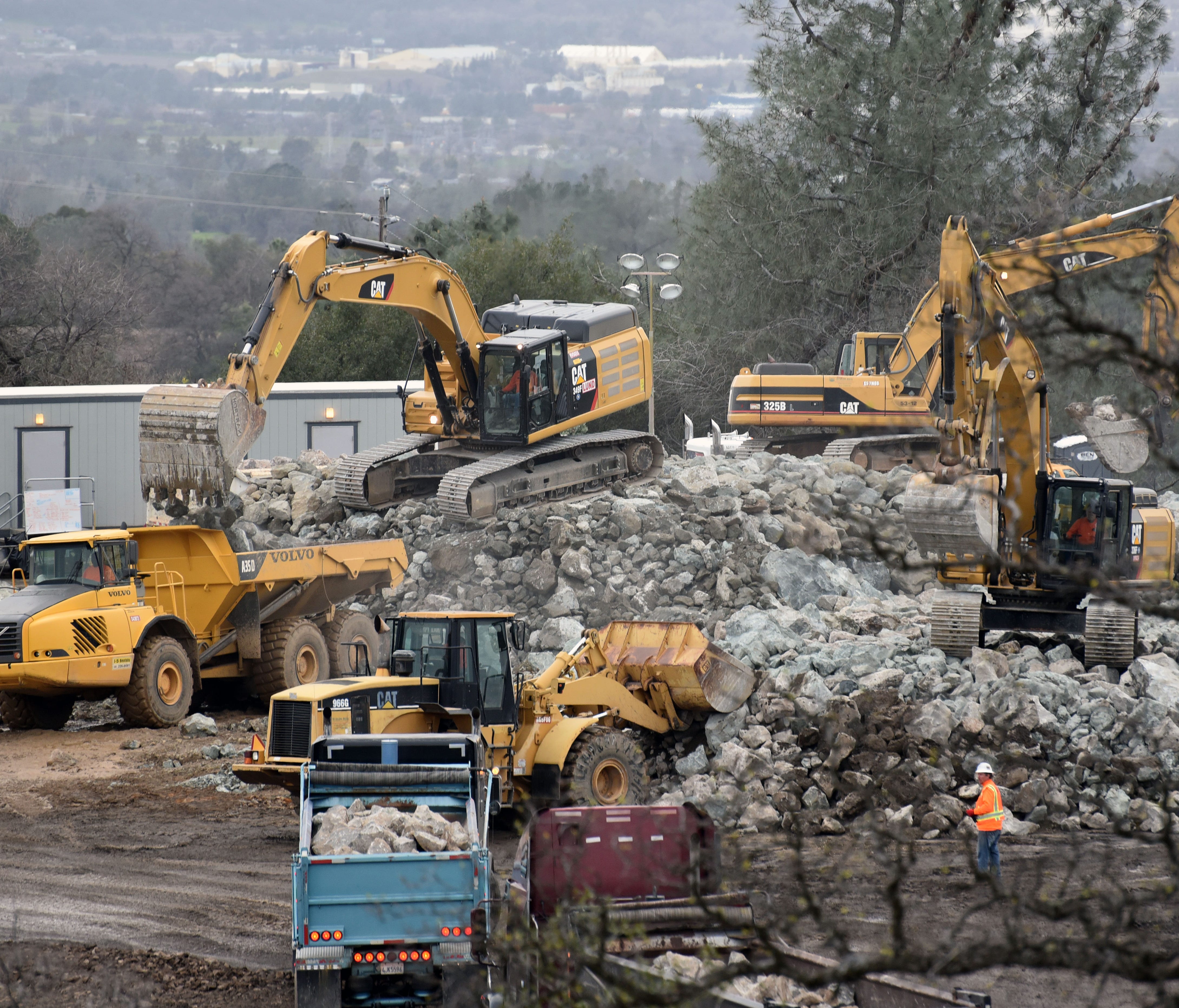 Contractors race to repair the Oroville Dam, with trucks delivering rocks, which are then loaded into dump trucks to be hauled across the top of the structure to be placed in weak spots.