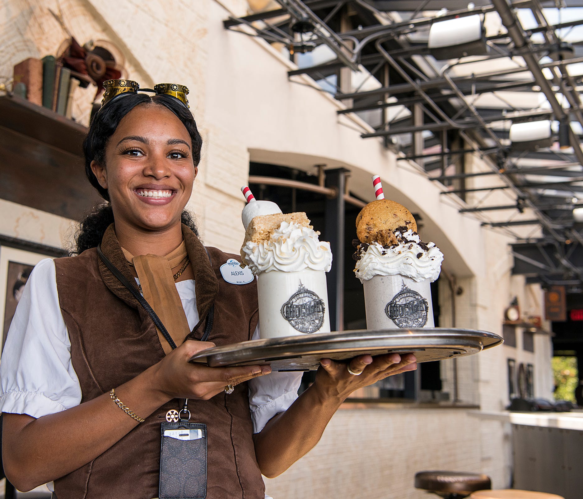 Alexis Thompson, a server at Toothsome Chocolate Emporium, displays two of the eatery's gargantuan milkshakes that highlight the menu. The Marshmallow Crisp includes a Kellogg's Rice Krispies treat, and the Cookie Jar includes cookie crumbles and a w