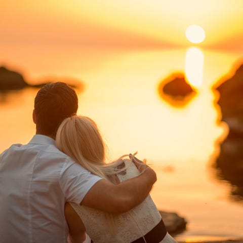 Couple blissfully staring at a sunrise over water