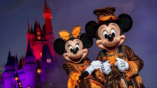 Mickey and Minnie in black-and-orange costumes in front of Cinderella's Castle.