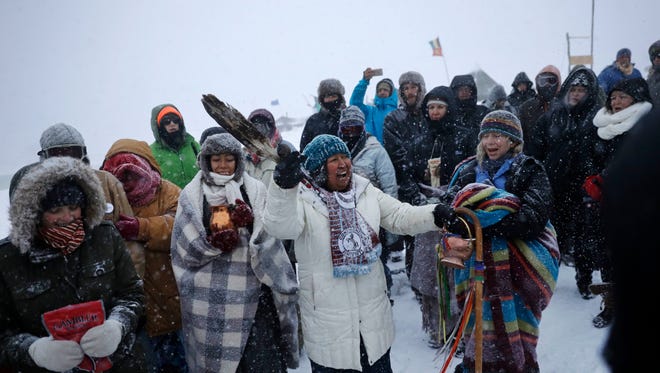 In this Tuesday, Nov. 29, 2016 photo, Beatrice Menase Kwe Jackson of the Ojibwe Native American tribe leads a song during a traditional water ceremony along the Cannonball river at the Oceti Sakowin camp where people have gathered to protest the Dakota Access oil pipeline in Cannon Ball, N.D. The pipeline is largely complete except for a short segment that is planned to pass beneath a Missouri River reservoir. The company doing the building says it is unwilling to reroute the project. (AP Photo/David Goldman)