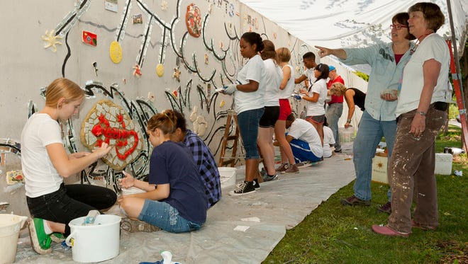 Brittney Flaten, 16, left of Ithaca, works to separate small mirrored tile sections as two of the six designers, Carla Stetson, of Candor, and Margaret Corbitt, right, of Danby, talk Friday morning during the creation of the 1st Street Mural in Ithaca. Two-years in the design stage, the mural’s theme is plants as food. The mural will eventually cover the entire length of the City of Ithaca's Water and Sewer Division's yard wall, opposite the Sciencenter. Helping with the work were six incoming Ithaca College students with the Community Plunge Jump Start program.