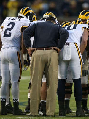 Michigan football coach Jim Harbaugh joins the huddle during the spring game April 1, 2016, at Michigan Stadium in Ann Arbor.