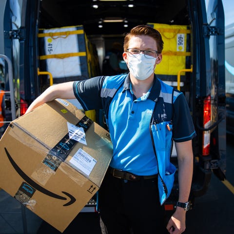A masked Amazon delivery driver holds a large pack