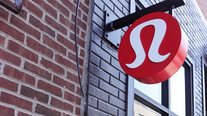 A sign of Lululemon's logo hanging outside of a brick building