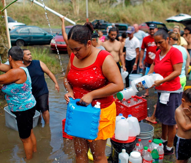 People collect water from a natural spring created by landslides in a mountain next to a road in Corozal, Puerto Rico, on Sept. 24, 2017.