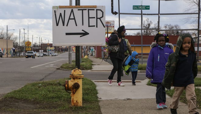 People walk along Saginaw St. on Flint's north side past a sign for water being given away at Mt. Calvary Missionary Baptist Church in Flint in March 2016. The church started handing out donated water from throughout the United States and Canada twice-a-week to people in need and small churches during the Flint water crisis.