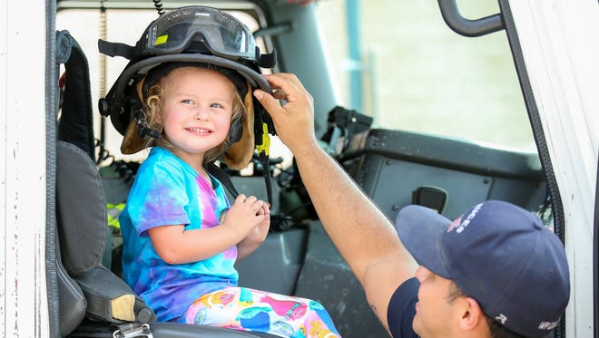 Olivia Weir, 3, of Las Cruces, gets a tour the  Las Cruces Fire Department's Truck 1  on Saturday, July 29, 2017, during the Parks and Recreation Department's "Kids EXPO 2017" at the Plaza de Las Cruces. Placing the helmet on the girl's head is firefighter Steve Gonzales.