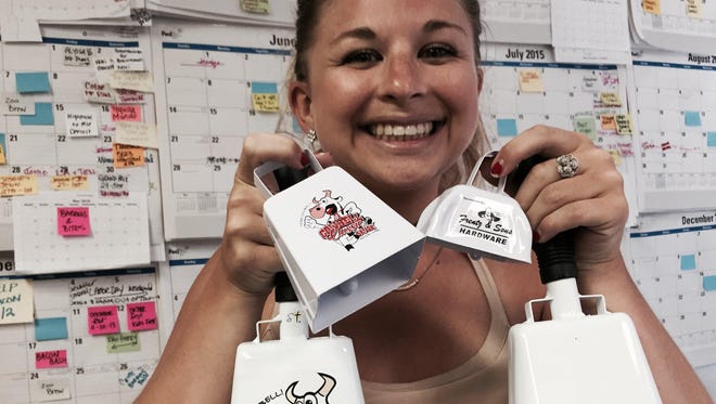 Alyssa Young, director for the Cowbell Classic races in Royal Oak, poses in her Ferndale office Monday with replicas of the cowbells that runners and their friends will use at the event on Saturday to try to break a Guinness World Records mark for "Largest Cowbell Ensemble."