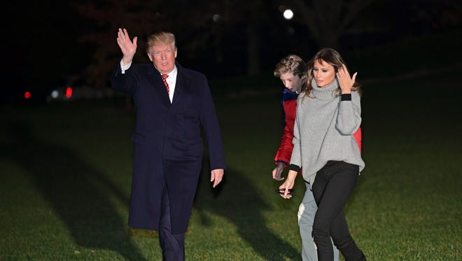 President Donald Trump, left, waves as he walks with first lady Melania Trump, right, and their son Barron Trump on the South Lawn of the White House in Washington, Sunday, Nov. 26, 2017, after returning from Palm Springs, Fla.