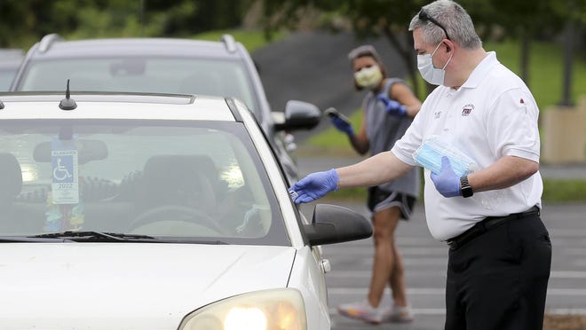 Members of the Tuscaloosa COVID-19 incident command team pass out masks during a drive-thru distribution at the Tuscaloosa Amphitheater Tuesday, July 7, 2020. Fire Chief and Incident Commander Randy Smith passes masks to a motorist.