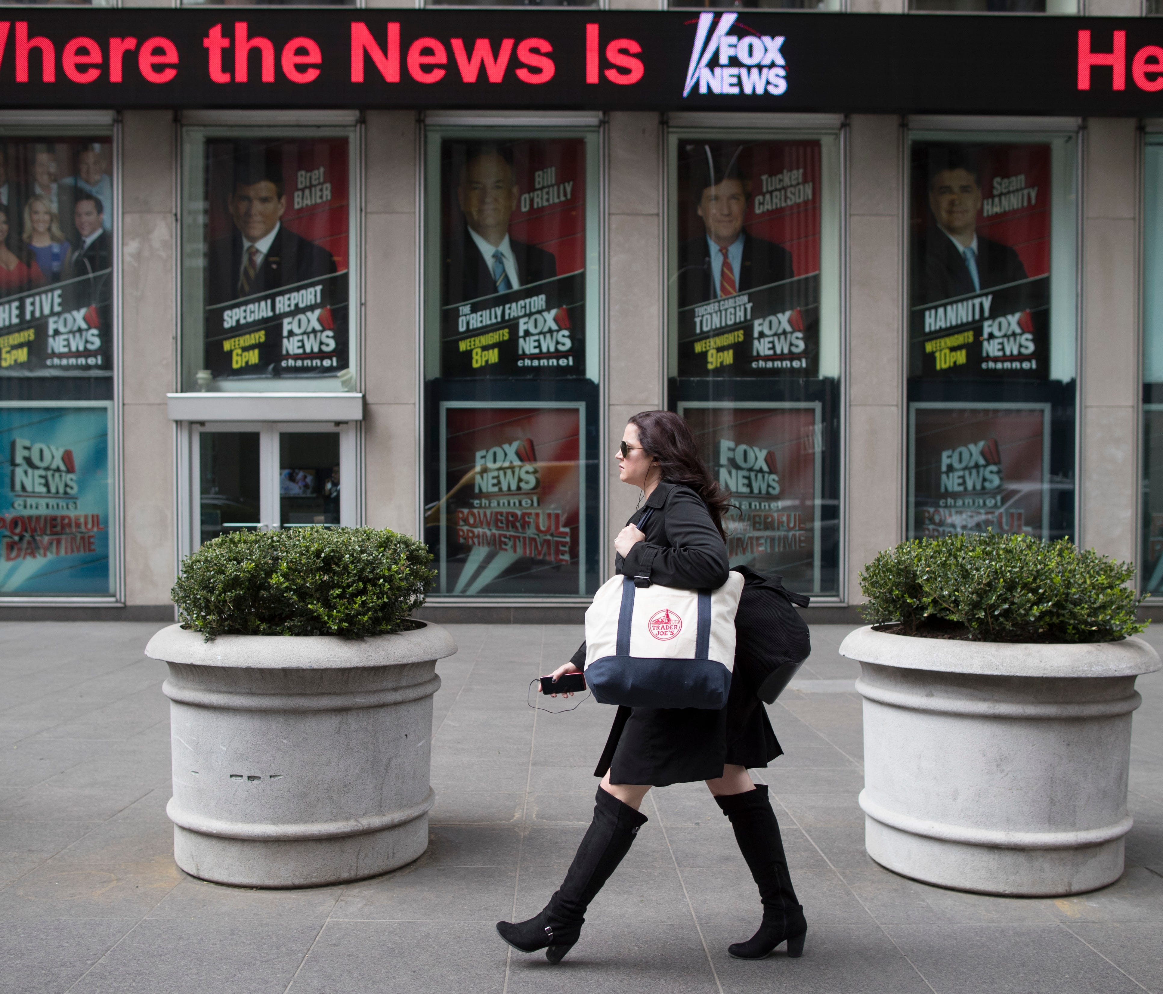 A woman walks past the News Corp. headquarters building displaying posters featuring Fox News Channel personalities including  Bill O'Reilly, top center, in New York, Wednesday, April 19, 2017. T
