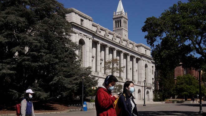 People wear masks while walking past Wheeler Hall on the University of California campus in Berkeley, Calif.