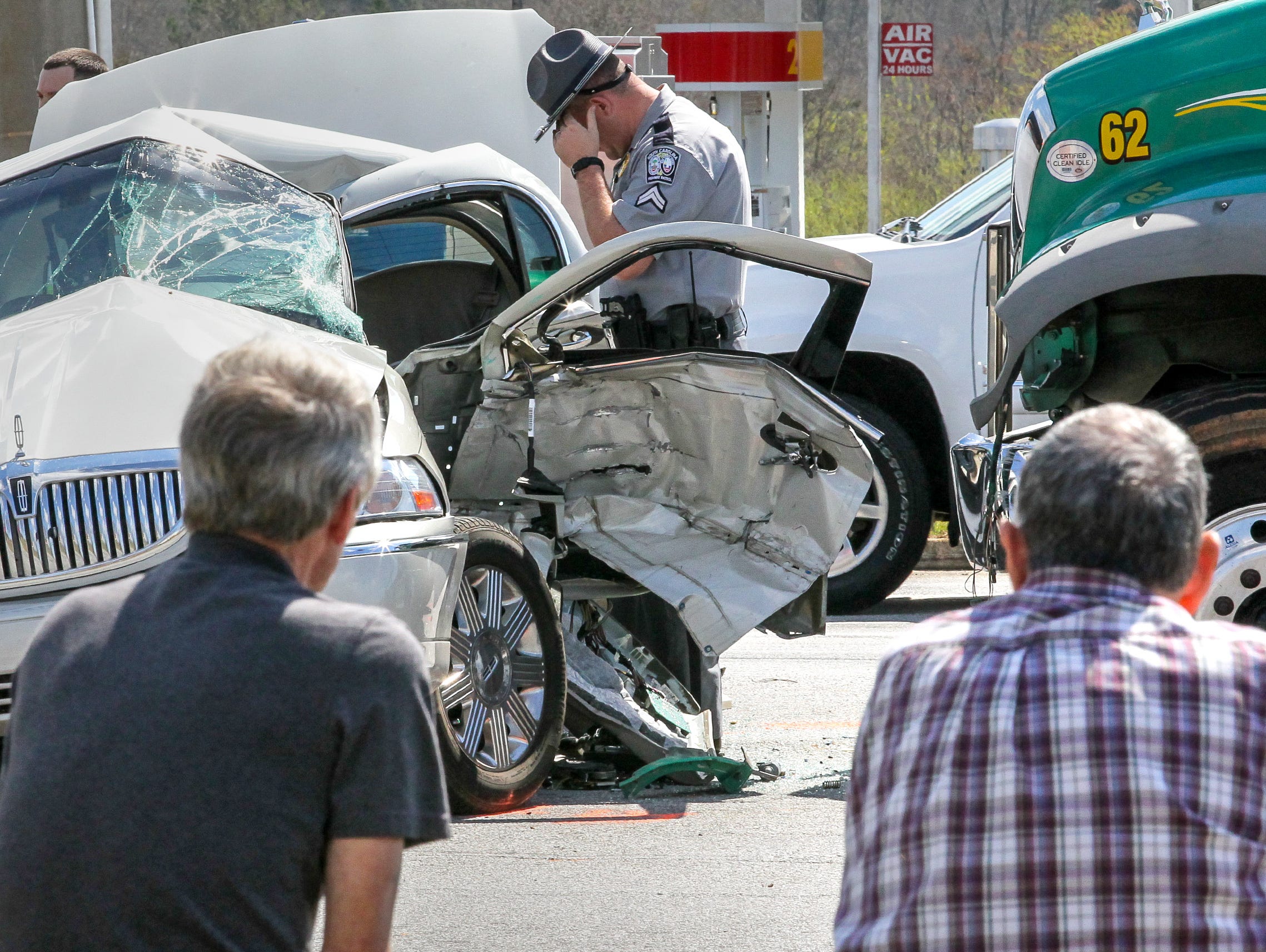 A South Carolina Highway Patrol officer looks over the scene of a wreck Friday afternoon at S.C. 24 and Whitehall Road. A Mack truck from Powell's Trash Services collided with a beige Lincoln Continental shortly after noon. The truck driver, left, wa