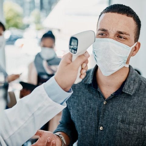 Traveler in face mask getting his temperature chec