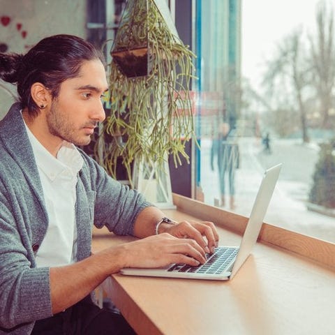 A man working on a laptop while sitting at a windo