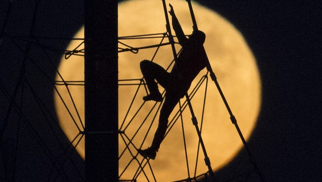 A man descends a pyramid net play structure while a supermoon rises behind him at Riverview Park in Mesa on Dec. 13, 2016.