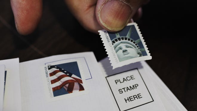 FILE - In this Dec. 5, 2011 file photo, a customer places first class stamps on envelopes at a U.S. Post Office in San Jose, Calif.