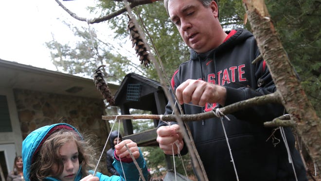 Lillian Goodsell, 6, ties up a pine cone bird feeder with the help from Jason Larson, the director of the park district at the Gorman Nature Center on Saturday. 