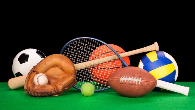 A collection of sports equipment suck as a football, basketball, baseball, tennin racquet, volleyball, soccer ball and catchers glove with a balck background.