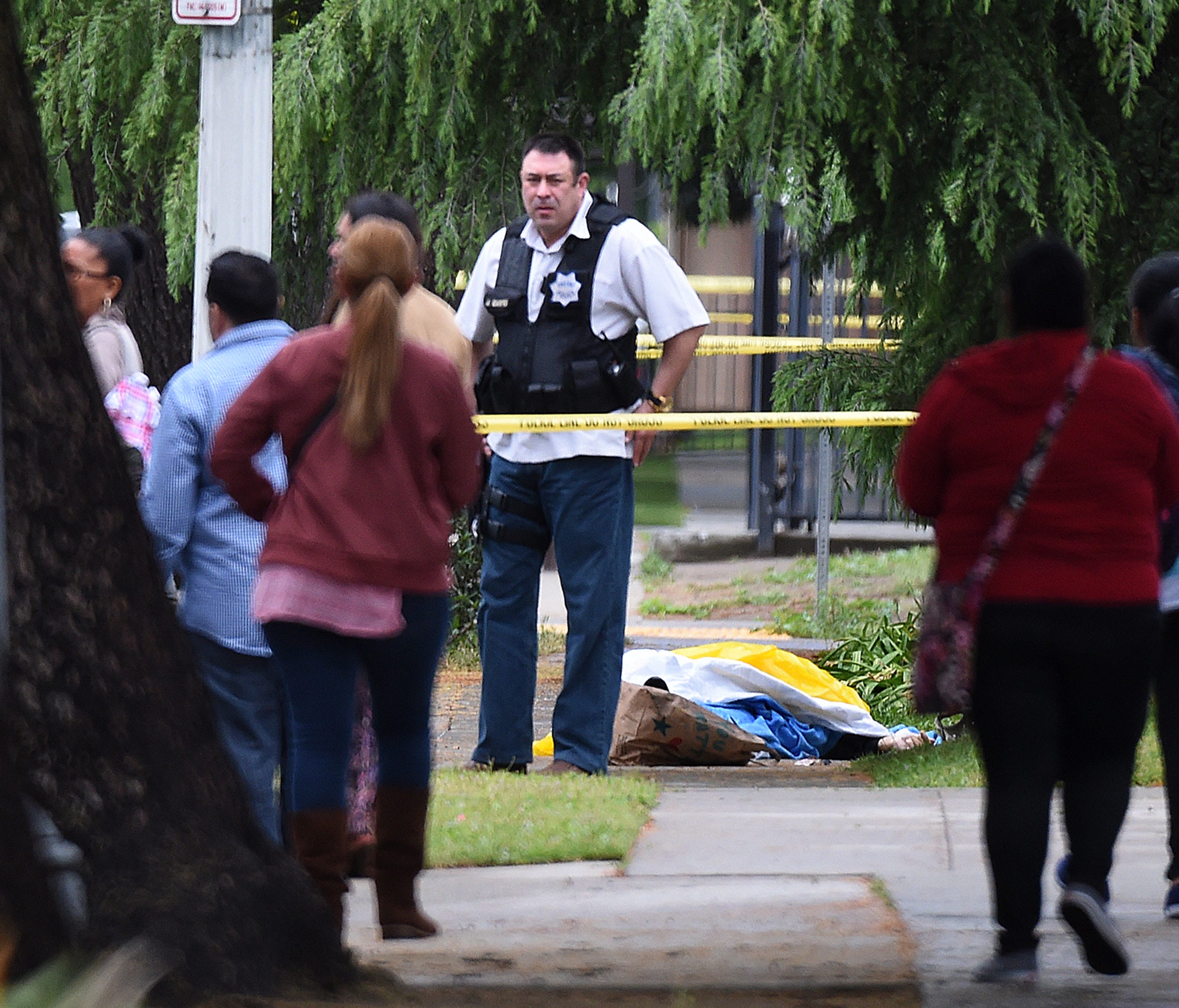 A Fresno police detective stands over the body of one of the three shooting victims Tuesday, April 18, 2017 in Fresno, Calif. A man shot and killed three people on the streets of downtown Fresno on Tuesday, shouting 