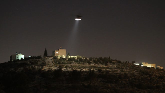 A picture taken from the Palestinian village of Dahriya shows an Israeli army helicopter patrolling a Jewish settlement.