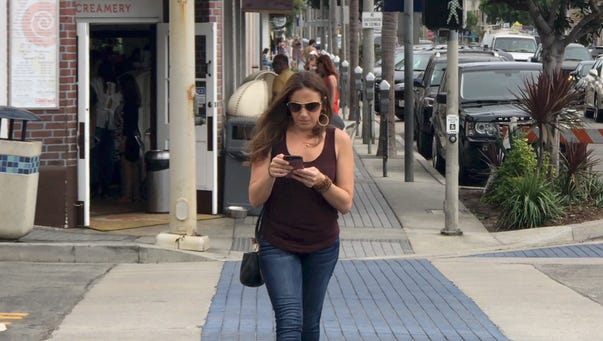 A woman checks out her cellphone while crossing the