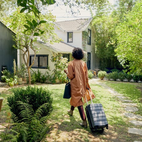 A person pulling a suitcase and walking up to an Airbnb residence.