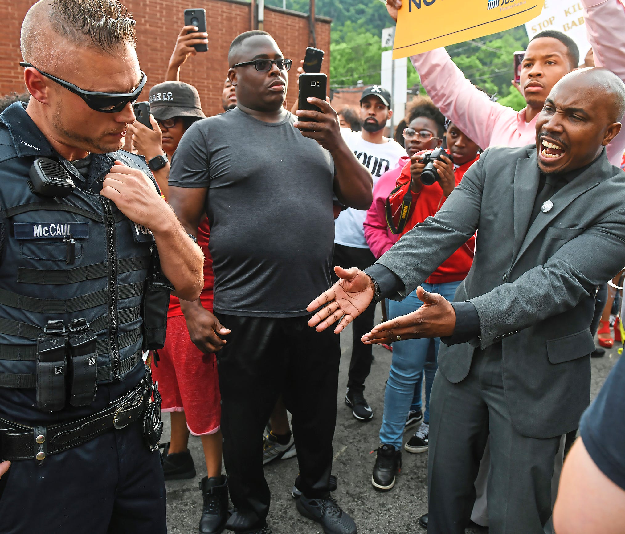 Leonard Hammonds II, of Penn Hills, right, points out that a Turtle Creek Police officer has his had on his weapon during a rally in East Pittsburgh, Pa., on Wednesday, June 20, 2018, at a protest regarding the shooting death of Antwon Rose by an Eas