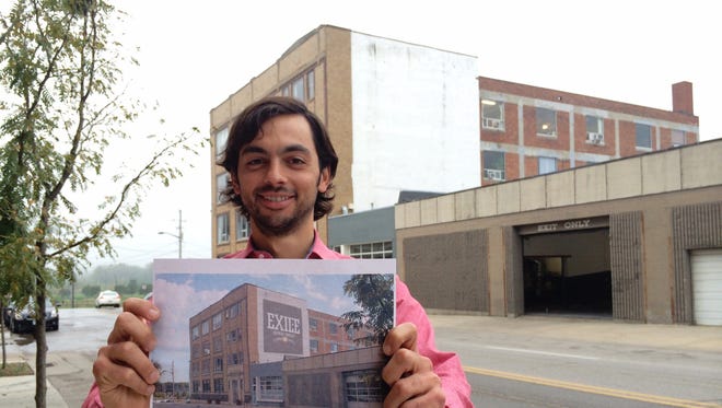 R.J. Tursi, owner of Exile Brewing Company, holds the digital image of a proposed painted advertisement for the white wall of the Fitch Studio Building, 304 15th Street, seen in background. City code opposes the sign because of its proximity to the Sculpture Park visible to the north.