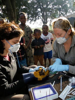 Tiziana Lembo (left) and Alison Peel take samples from bats while children watch in Morogoro, Tanzania. The researchers gather data in the field — everything from the size and frequency of bat litters, to the levels of virus in their blood serum — in an effort to build mathematical tools that will help scientists predict an infectious outbreak.