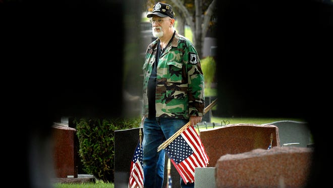 Vietnam Veteran Tom Demerath, of Green Bay, is framed through a gravestone as he places American flags on the gravesites to honor our fallen heros for Memorial Day at Allouez Catholic Cemetery.