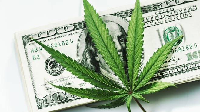 Marijuana leaf on top of a pile of $100 bills.