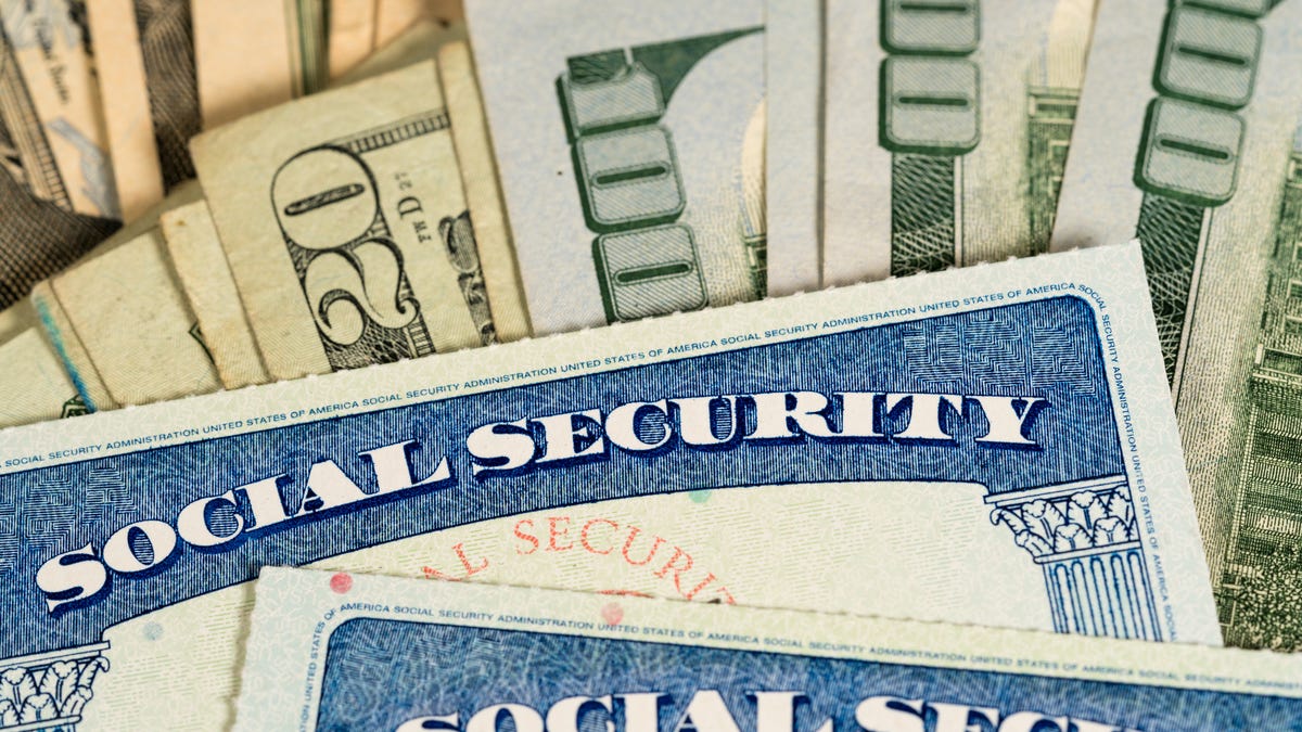 Two Social Security cards lying atop a fanned pile of cash.