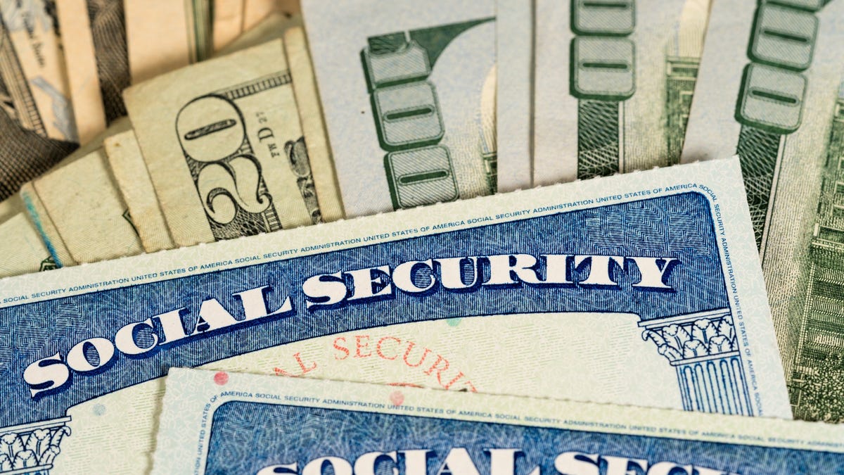Two Social Security cards lying atop a fanned pile of cash