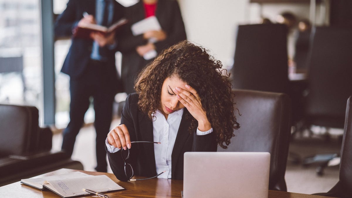 Stressed female employee with hand on forehead and bosses in the background