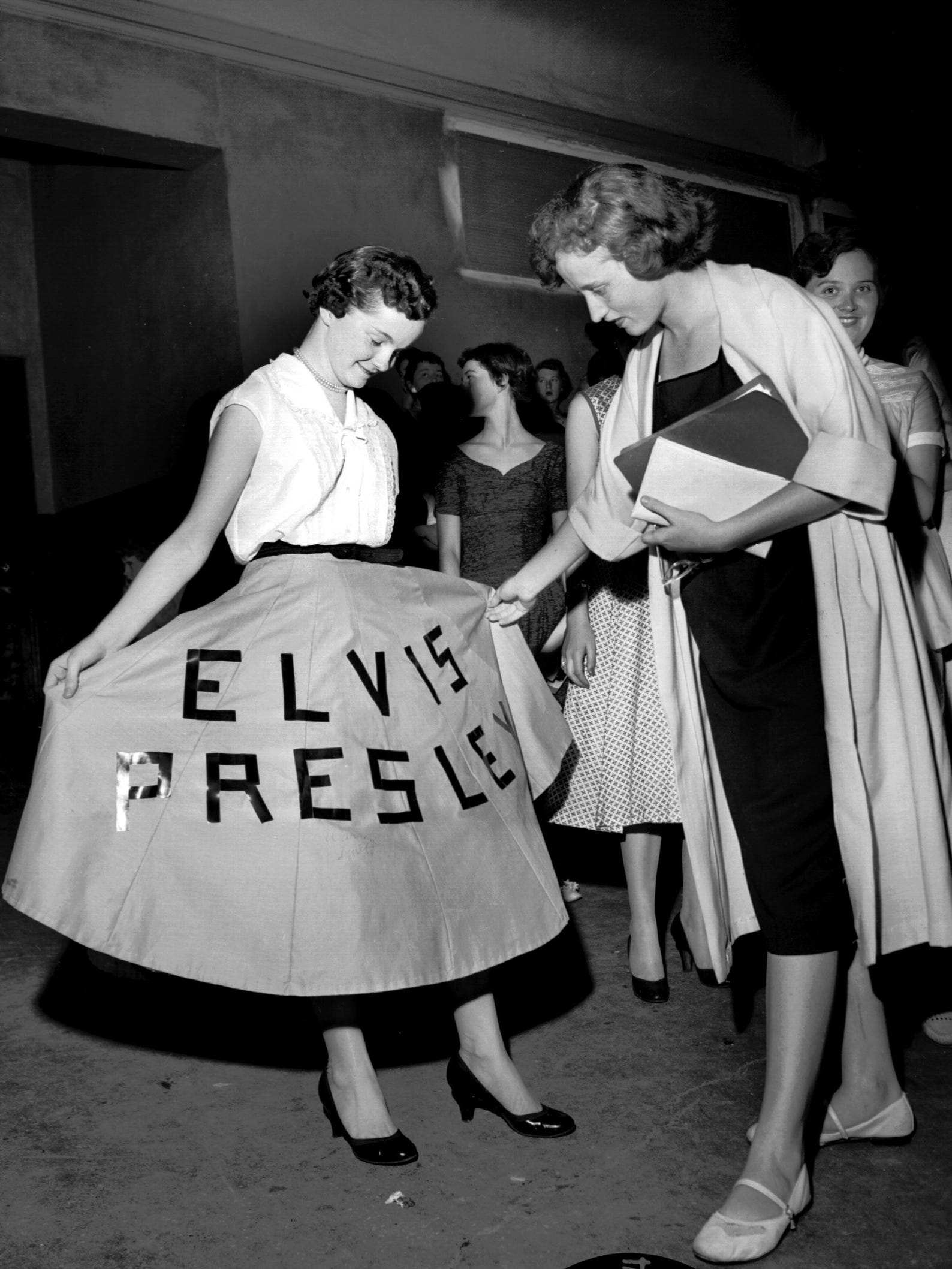A fan shows off her dress at Elvis Presley's concert at Ellis Auditorium in 1956. More than 7,000 people jammed Ellis Auditorium on the night of May 15 to stomp, shudder, shriek and sigh as a young Elvis writhed his way through a rock 'n' roll repertoire. He was the blockbuster of Bob Neal's Cotton Picking Jamboree, a feature of Cotton Carnival opening night.
