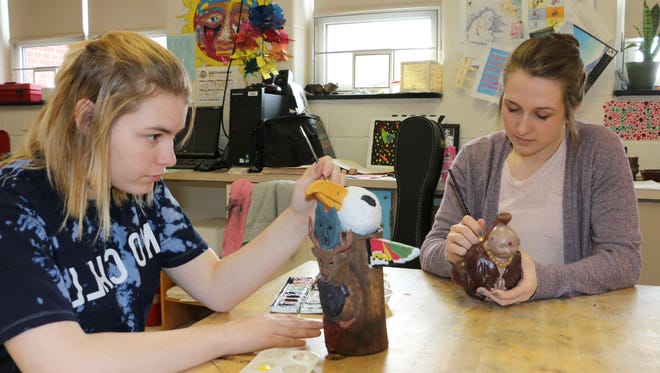 Putting the finishing touches on the ceramic musical instruments they have created from stoneware clay and acrylic paint are Vera Pieri, left, an 11th-grader who is making a totem pole whistle, and Lauren Smith, a 12th-grader who is working on her Buddha whistle. They are students in James States' art class at North Penn-Mansfield High School. Both have submitted photographs of their whistles to the Gmeiner for consideration for the youth exhibit.