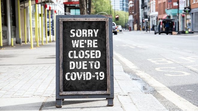 A sandwich board on a sidewalk that reads Sorry We're Closed Due to COVID-19.