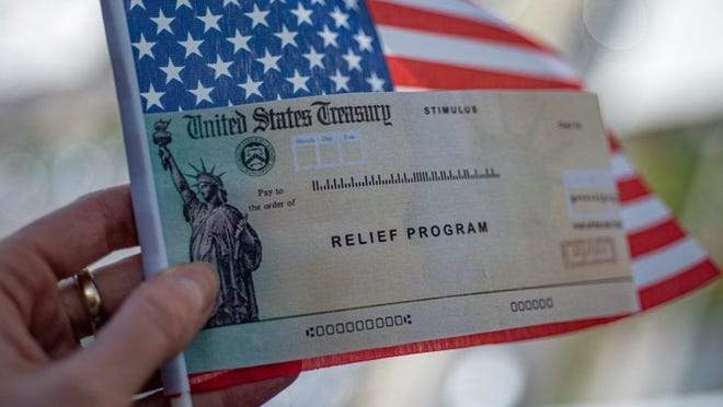 A hand holding a small American flag and a stimulus check from the U.S. Treasury.